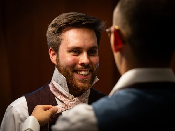 Adam and Abbey’s wedding at Tottington Manor – groom smiling as his cravat is tied