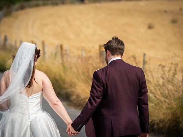 Adam and Abbey’s wedding at Tottington Manor – couple walking hand in hand by the fields