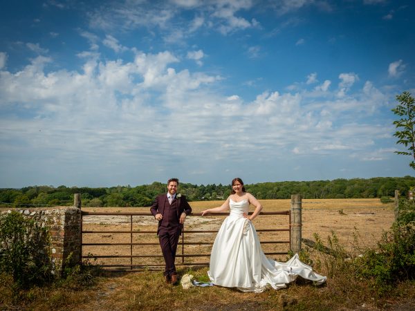 Adam and Abbey’s wedding at Tottington Manor – couple at a field gate under a big sky