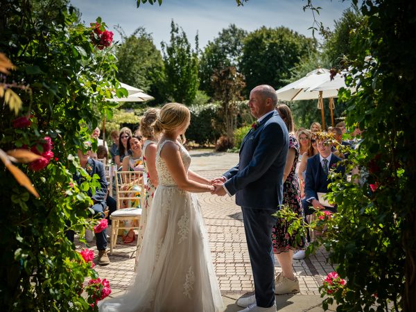 Holly and Andy’s wedding at Field Place – bride and groom under the rose arch