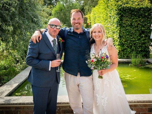 Holly and Andy’s wedding at Field Place – bride and groom with a guest by the lily pond